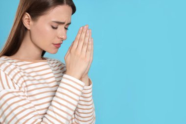 Woman with clasped hands praying on turquoise background, space for text