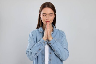 Woman with clasped hands praying on light grey background