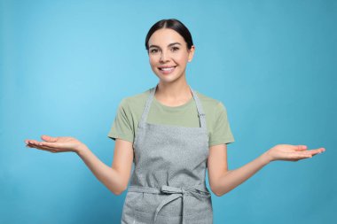Young woman in grey apron on light blue background,