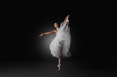 Young ballerina practicing dance moves on black background