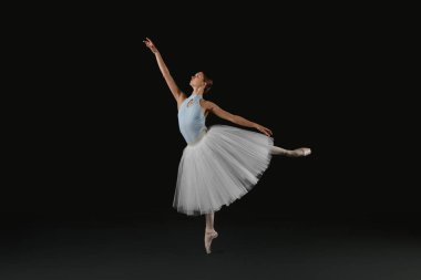 Young ballerina practicing dance moves on black background