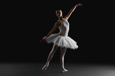 Young ballerina practicing dance moves on black background