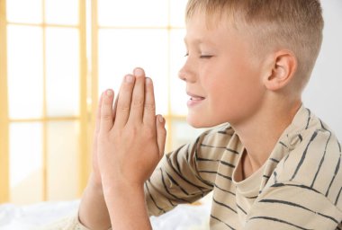 Boy with clasped hands praying indoors, space for text