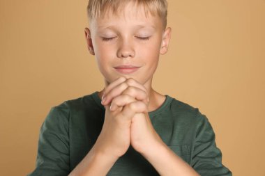 Bej arka planda dua eden elleri sımsıkı bağlı bir çocuk