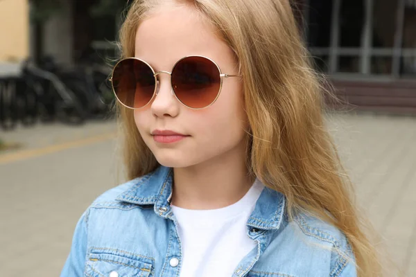 Girl wearing stylish sunglasses on street near building
