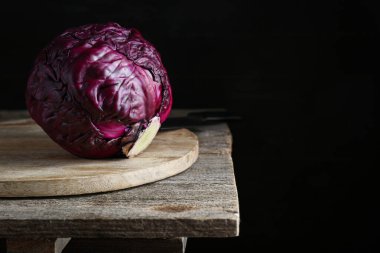 Fresh ripe red cabbage on wooden table against dark background. Space for text