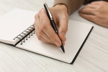Man writing in notebook at white wooden table, closeup