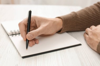 Man writing in notebook at white wooden table, closeup