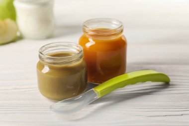 Jars with healthy baby food and spoon on white wooden table