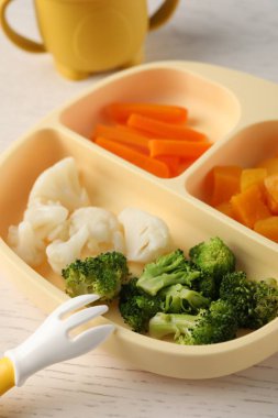 Baby food. Section plate with different vegetables on white wooden table, closeup