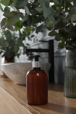 Soap bottle and eucalyptus branches near vessel sink on bathroom vanity. Interior design