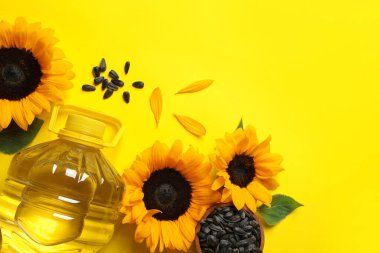 Bottle of cooking oil, sunflowers and seeds on yellow background, flat lay