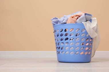 Laundry basket with clothes near beige wall indoors. Space for text