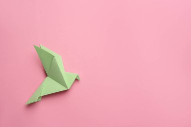 Beautiful light green origami bird on pink background, top view. Space for text