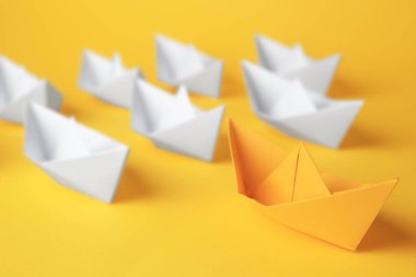 Group of paper boats following yellow one on color background. Leadership concept