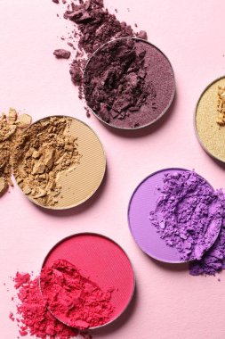 Different crushed eye shadows on pink background, flat lay