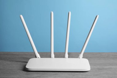 New white Wi-Fi router on wooden table against light blue background