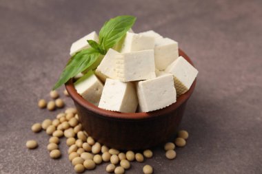 Delicious tofu cheese, basil and soybeans on brown textured table, closeup