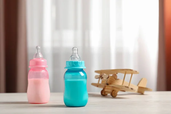 Feeding bottles with milk and toy plane on white wooden table indoors