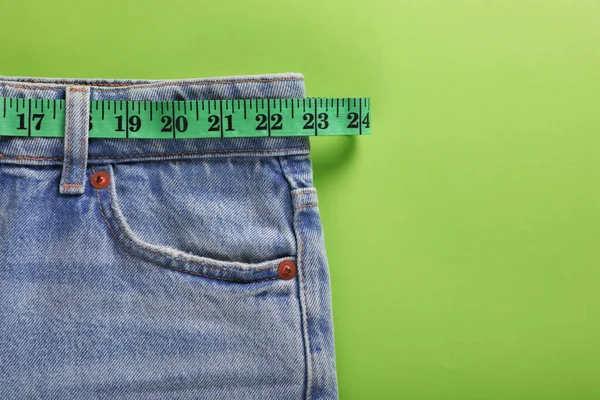 Jeans and measuring tape on light green background, top view with space for text. Weight loss concept