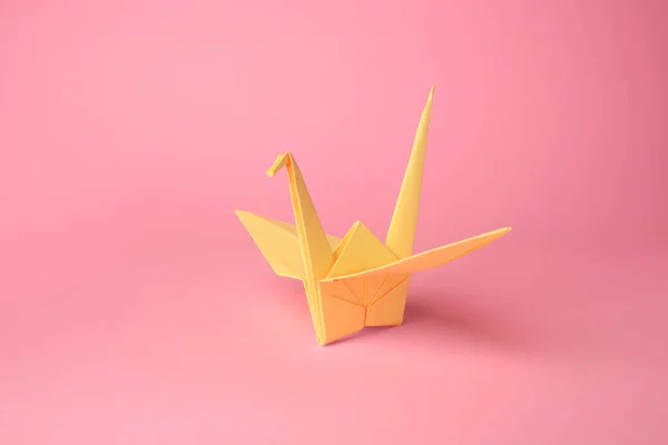 Origami art. Handmade paper crane on pink background