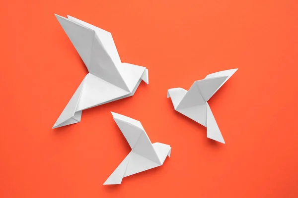 Beautiful white origami birds on orange background, flat lay