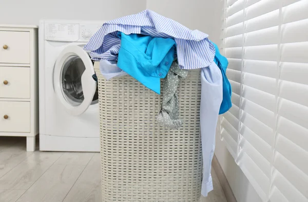 Plastic laundry basket overfilled with clothes in bathroom