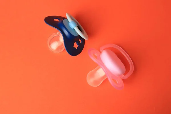 Colorful baby pacifiers on orange background, flat lay