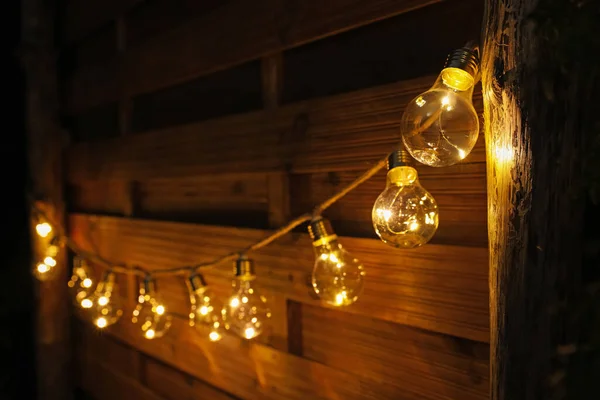 Garland of lamp bulbs hanging on wooden wall. String lights