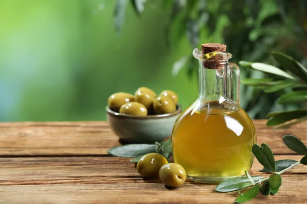 Jug of cooking oil, olives and green leaves on wooden table. Space for text