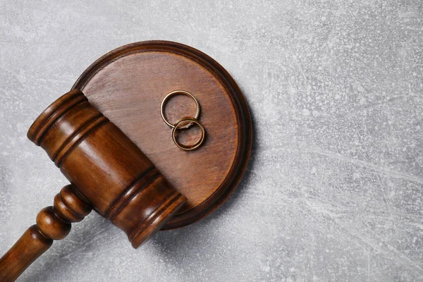 Divorce process. Wooden gavel and wedding rings on grey textured table, top view. Space for text