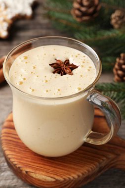 Glass of delicious eggnog with anise star on wooden table, closeup