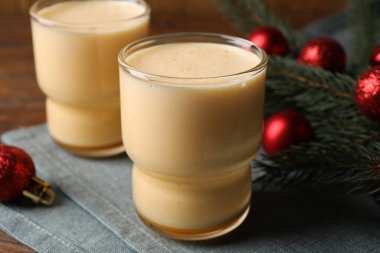 Glasses of delicious eggnog and decorated fir branch on wooden table, closeup