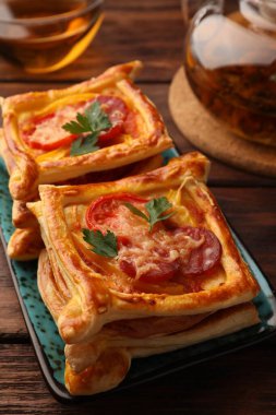 Fresh delicious puff pastry with cheese, tomatoes and parsley on wooden table, closeup