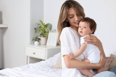 Mother hugging her cute little baby in bedroom, space for text