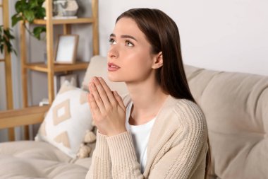 Ellerini kenetlemiş evde dua eden bir kadın.