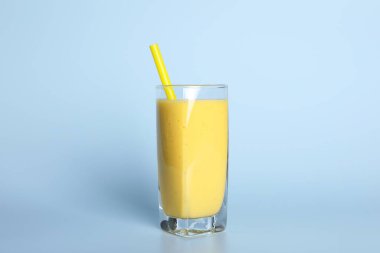 Açık mavi arkaplanda saman bulunan bir bardak lezzetli smoothie.