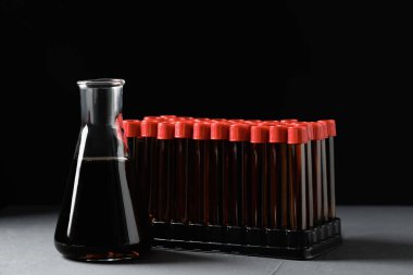 Different laboratory glassware with brown liquid on grey table against black background