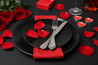 Beautiful table setting with burning candles and bouquet on black table for romantic dinner