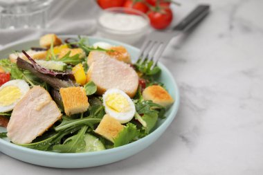 Delicious salad with croutons, chicken and eggs served on white marble table, closeup. Space for text