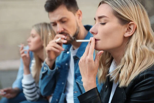 People smoking cigarettes at public place outdoors, closeup