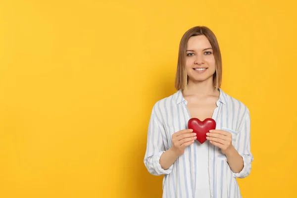 Young Woman Holding Red Heart Yellow Background Space Text Volunteer — Stockfoto