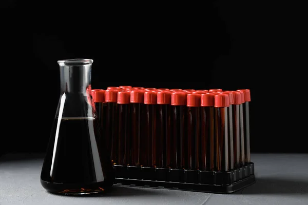 Different laboratory glassware with brown liquid on grey table against black background