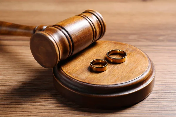 Divorce process. Gavel and wedding rings on wooden table, closeup
