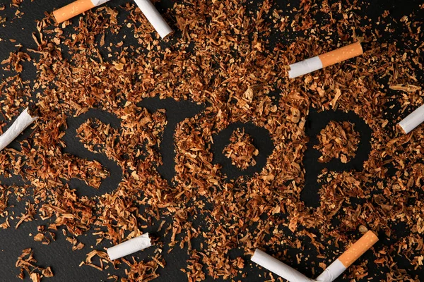 Word Stop made of dry tobacco and broken cigarettes on dark grey background, flat lay. Quitting smoking concept