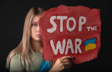Sad woman holding poster with words Stop the War on black background