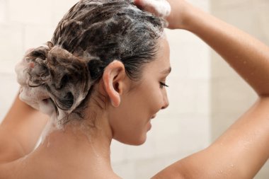 Evde duş alırken saç yıkayan genç bir kadın.