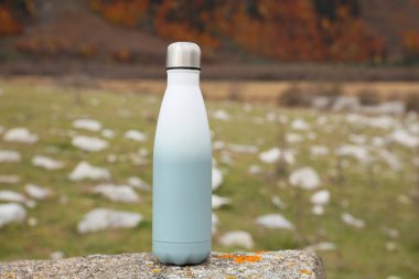 Thermo bottle on rock in mountains. Space for text