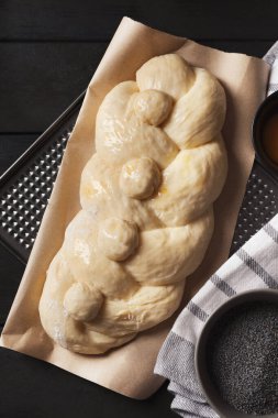 Çiğ ekmek ve haşhaş tohumlarını siyah ahşap masada düz bir şekilde ördüm. Geleneksel Şabat challah