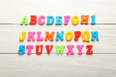 Beyaz ahşap masanın üzerinde düz, renkli manyetik harfler var. Alfabetik sırayla